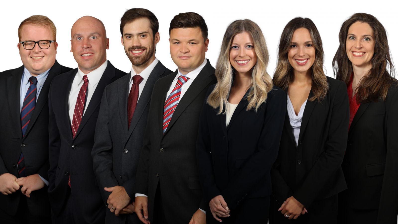A group of seven business professionals standing side-by-side in formal business attire against a white background.