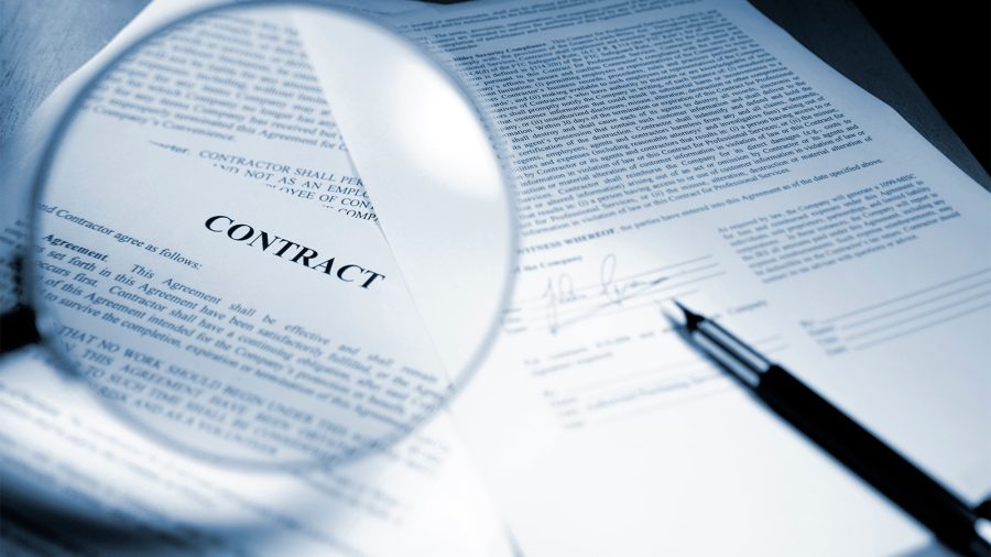 A close-up blue-toned image of a magnifying glass held out in front of page in a legal contract document.
