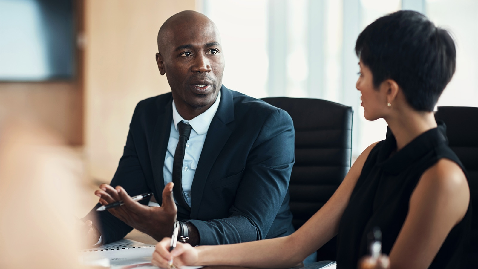 Black professional man discussing litigation matter with white professional female colleague in a corporate conference room