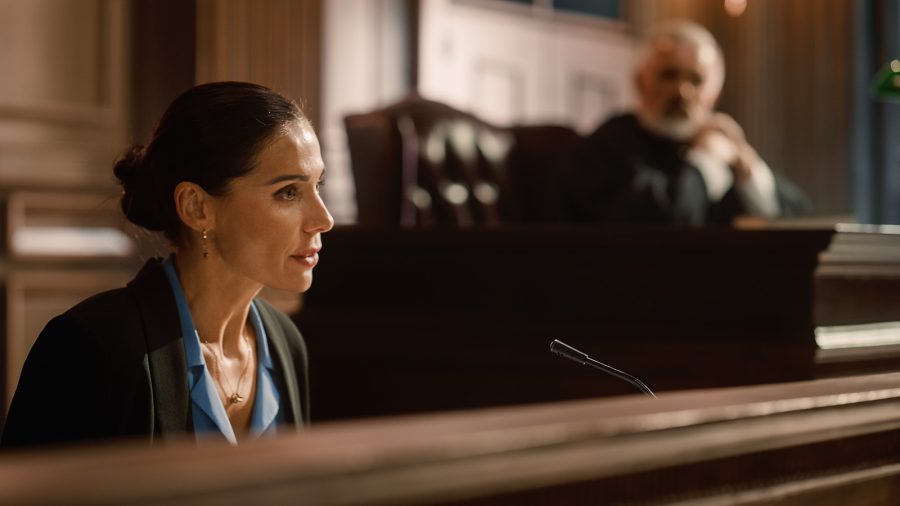 Female expert witness testifying in a court proceeding with the judge in the background listening to the testimony.