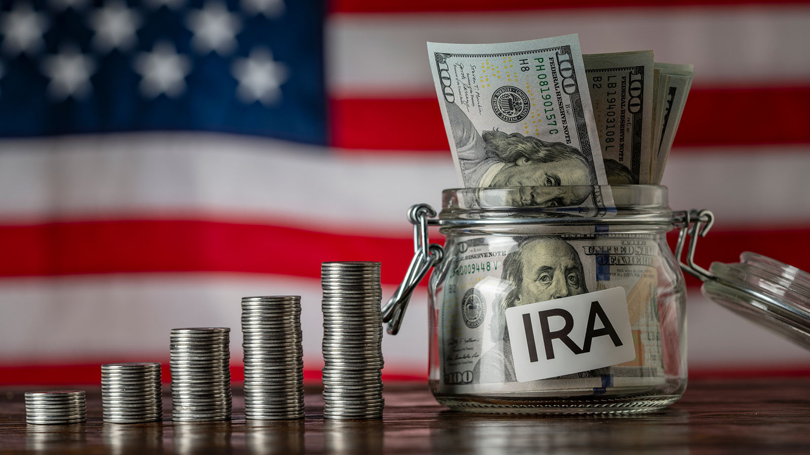 Money towers and glass jar used for saving US dollar bills and notes for IRA retirement fund on the American flag background, close up