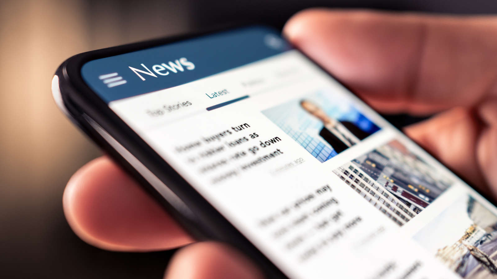 A person holds a smartphone displaying a digital news app, with headlines and images visible on the screen. The focus is on the phone, and the users hand is partially shown.