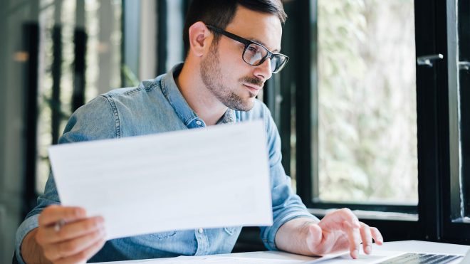 Man in his office looking at and working with laptop and papers and documents